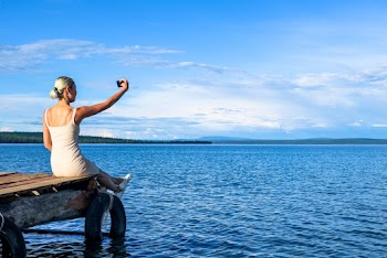 Woman Taking Selfie While Sitting on Brown Dock Outdoor