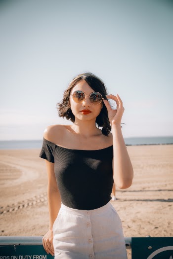 Woman Touching Her Sunglasses While Leaning on Gray Metal Bar