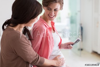 Woman touching stomach of pregnant friend holding ultrasound