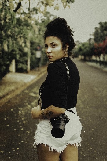 Woman Using Black Top and White Short Shorts With Camera on Her Shoulder on Road