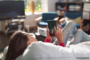 Woman using digital tablet on sunny sofa