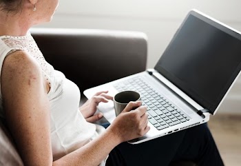 woman using laptop while holding mug