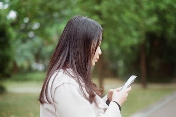 woman using phone standing beside tree