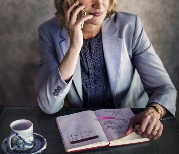 Woman Using Smartphone White Holding Opened Book Beside Ceramic Mug on Table