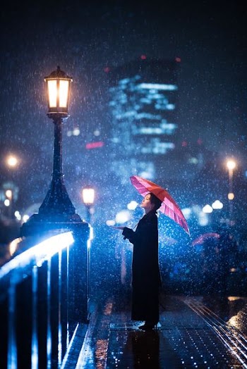woman using umbrella standing near bridge light post