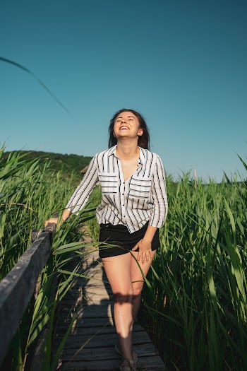 Woman Walking Along Wooden Footbridge Between Grasses