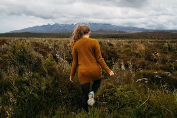 woman walking in grass field under stratocomulus clouds