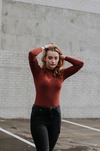 woman walking while holding her hair near brick wall during daytime