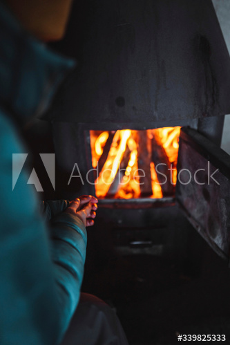 Woman warming up near a fireplace in a hut
