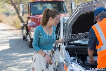 Woman watching male roadside assistance mechanic fix car at roadside