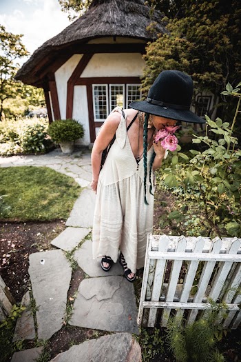 Woman Wearing a Black Hat Smelling a Flower Infront of a Gazebo