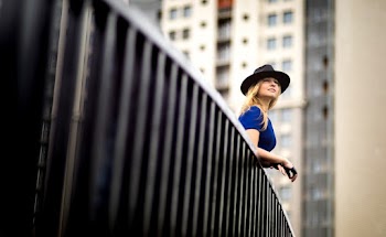 Woman wearing a blue top and a hat leaning on metal railing