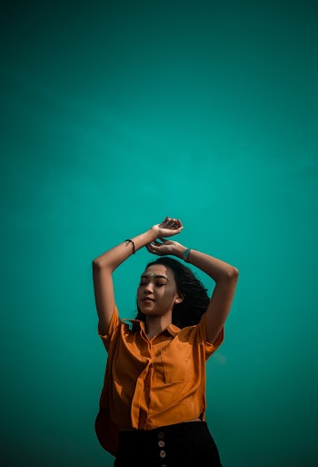 Woman Wearing an Orange Button-up Shirt Raising Her Arms above Her Head