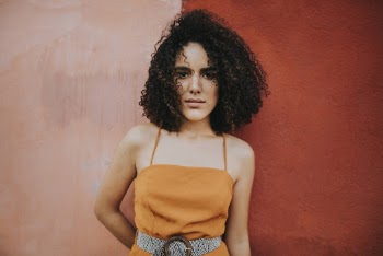Woman wearing an orange top standing beside pink wall