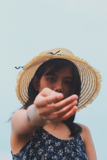 Woman Wearing Black and Blue Floral Sleeveless Top and Brown Hat Raising Right Hand