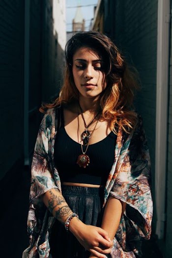 woman wearing black and multicolored shirt and cardigan standing on narrow pathway between buildings photo