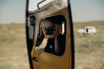 Woman Wearing Black and White Crew-neck T-shirt Sitting Inside Vehicle While Taking Photo on Green Field