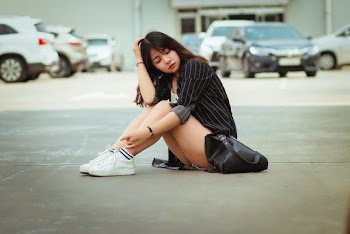 Woman Wearing Black-and-white Dress Shirt and Gray Shorts Sitting on Parking Lot