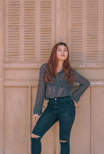 Woman Wearing Black and White Sports Shirt and Distressed Black Denim Jeans While Leaning on Wooden Wall