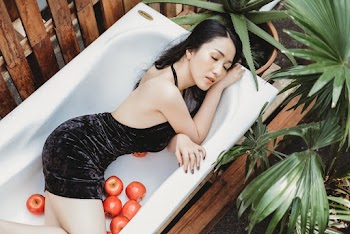 Woman Wearing Black Backless Dress Laying on White Bathtub