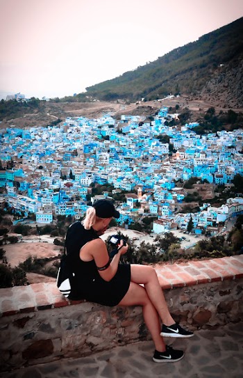 Woman Wearing Black Baseball Cap Sitting Near Blue and White Building Under White Clouds during Daytime