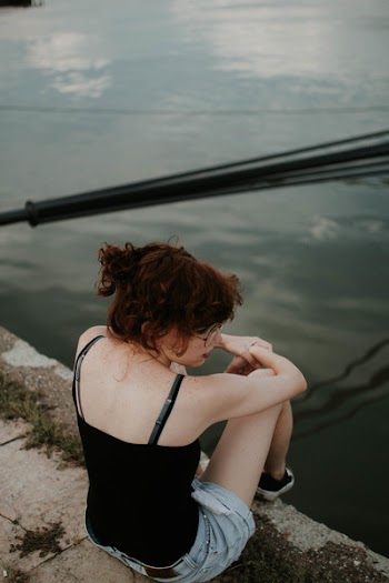 Woman Wearing Black Cami-top Sitting on Concrete Surface Near Body of Water
