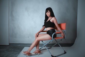 Woman Wearing Black Camisole and Short Shorts Sitting on Orange Director's Chair