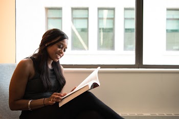 Woman Wearing Black Crew-neck Sleeveless Top Sitting of Gray Sofa While Reading Book