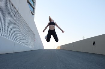 Woman Wearing Black Crop Top Jumping Beside the Building