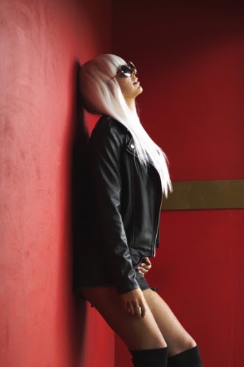 Woman Wearing Black Leather Jacket Leaning On Red Wall