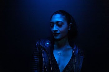 woman wearing black leather jacket leaning on wall under blue neon lights