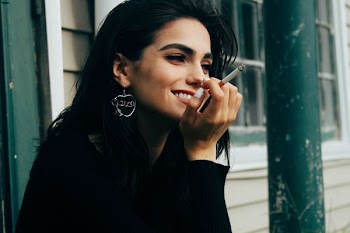 woman wearing black long-sleeved shirt holding lighted cigarette while smiling