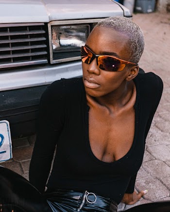 Woman wearing black scoop-neck long-sleeved shirt sitting down in front of parked vehicle
