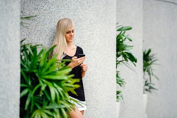 Woman Wearing Black Scoop-neck Shirt Standing in Front on Concrete Column Holding Smartphone