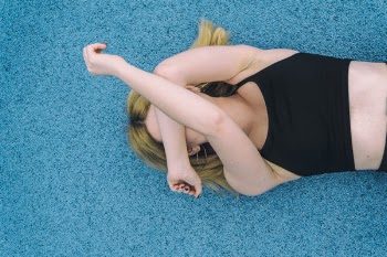 Woman Wearing Black Sports Brassiered Lying on Teal Surface While Covering Her Face With Her Arms