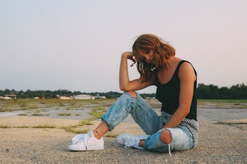 Woman Wearing Black Tank Top and Distressed Blue Denim Jeans Sits on Ground