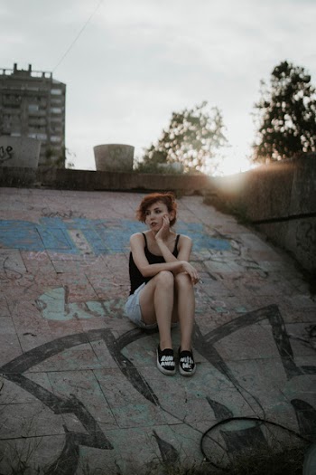 Woman Wearing Black Tank Top Sitting on Concrete Surface