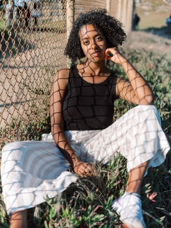 Woman Wearing Black Tank Top Sitting on Grass Beside Brown Cyclone Fence