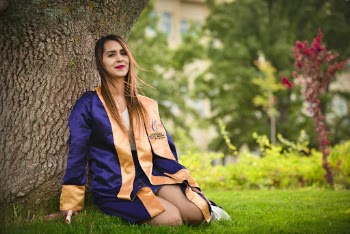 Woman Wearing Blue and Orange Academic Dress Sitting on Green Grass Field