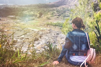 Woman Wearing Blue Denim Jacket Sitting on Cliff Overlooking Open Field