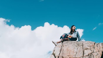 Woman Wearing Blue Denim Jacket Sitting on Top of A Rock