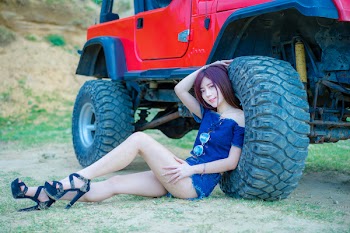 Woman Wearing Blue Off-shoulder Blouse and Blue Denim Short Shorts Sitting Near Red Truck