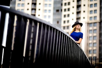 Woman wearing blue top and a hat leaning on metal railing