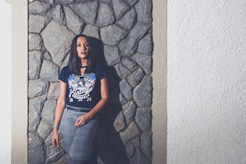 Woman Wearing Blue Wings-printed V-neck T-shirt and Gray Pants Leaning on Gray Rock Cladding