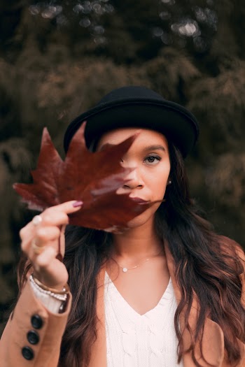 Woman Wearing Brown Coat and Black Hat While Holding Brown Maple Leaf