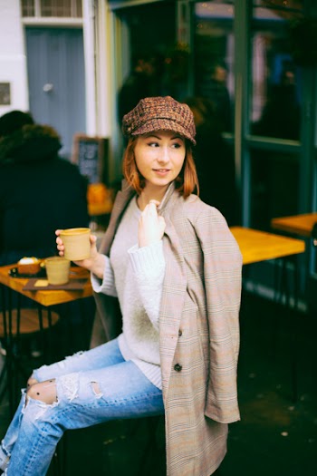 Woman Wearing Brown Coat Holding Cup Sitting on Chair