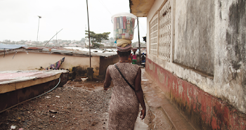 Woman Wearing Brown Dress Carrying A Plastic Container On Her Head