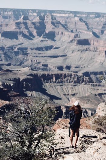 woman wearing cap standing near tree facing mountain during daytime