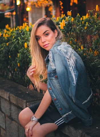 Woman Wearing Denim Jacket Sitting on Fence Next to Flowers