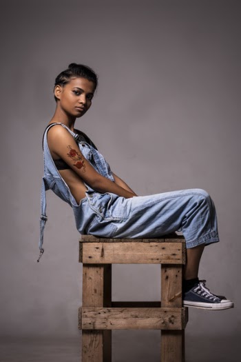 Woman Wearing Dungarees Sitting On Wooden Stool